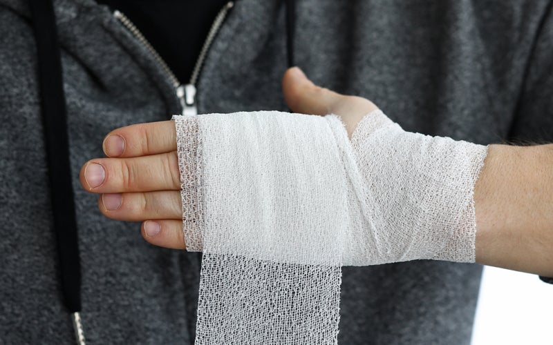 A person's hand and wrist being wrapped with a white gauze bandage.