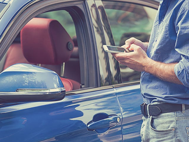 Person using a smartphone next to a blue car, possibly interacting with a car-related app.