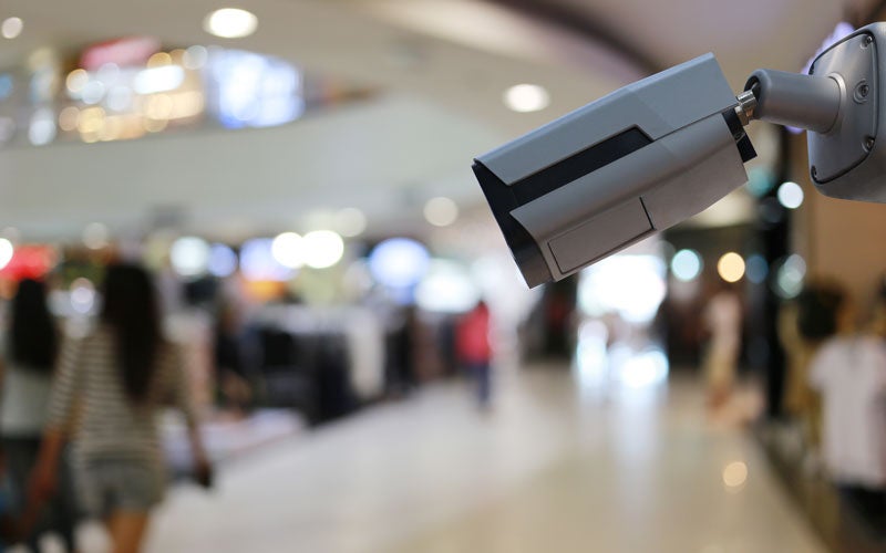 Security camera monitoring a blurred shopping mall with people walking.