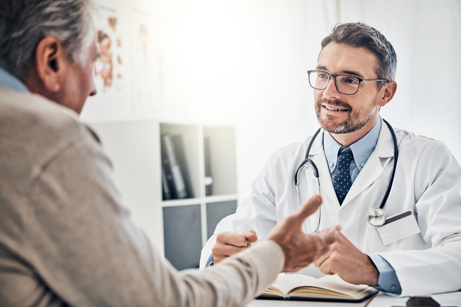 A smiling doctor in a white coat and stethoscope talks to a patient.