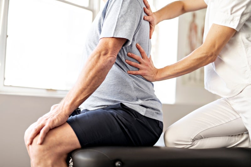 A healthcare professional examining an older patient's back on an exam table.