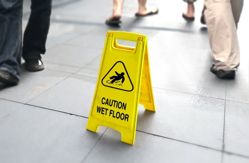 Yellow 'CAUTION WET FLOOR' sign on a wet tiled floor with blurred people walking past in the background.
